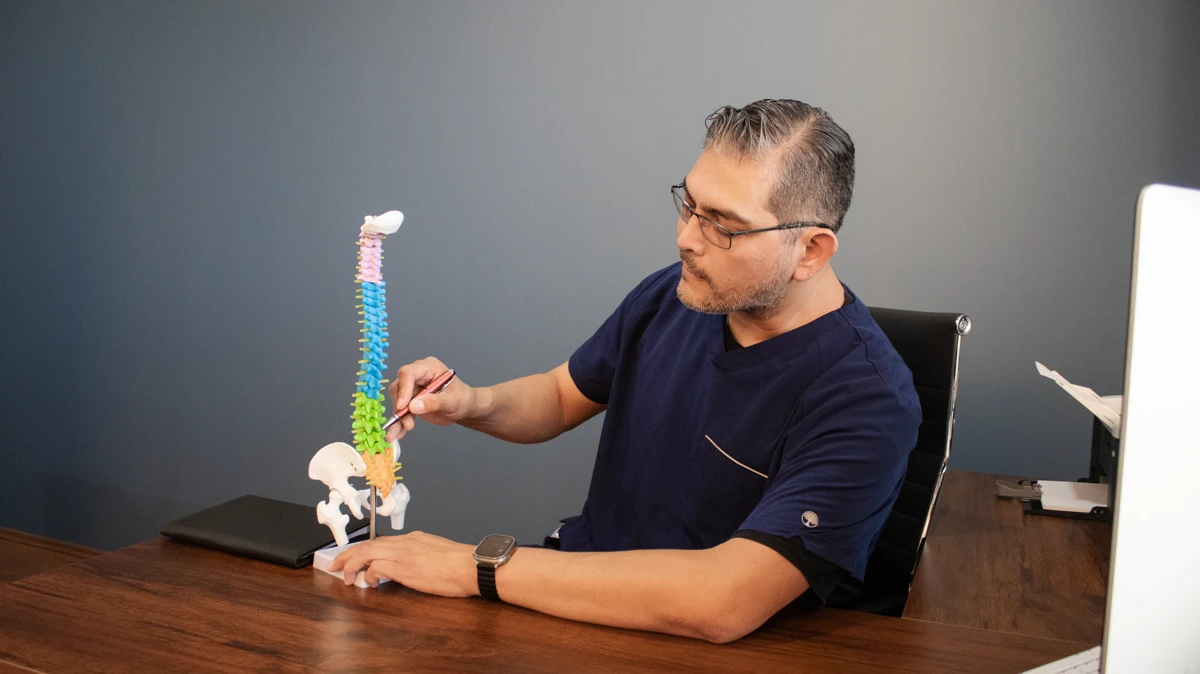 El Dr. Daniel Santana López explica la columna vertebral con un modelo anatómico durante la consulta