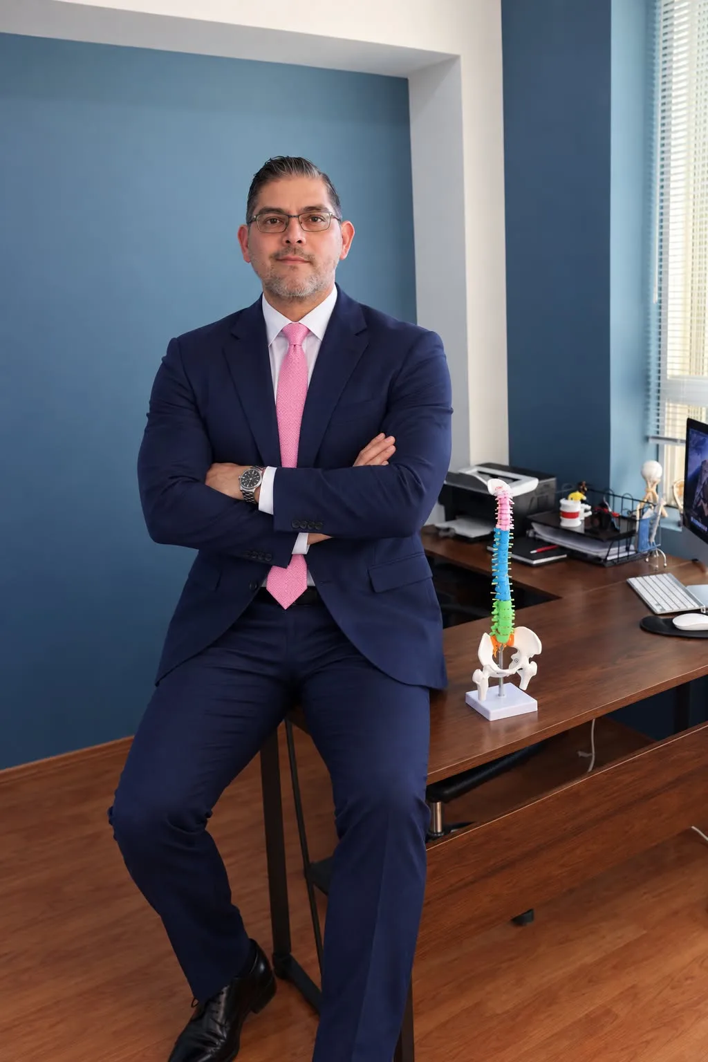 Dr. Daniel Santana López en su consultorio, junto a un modelo anatómico de columna vertebral